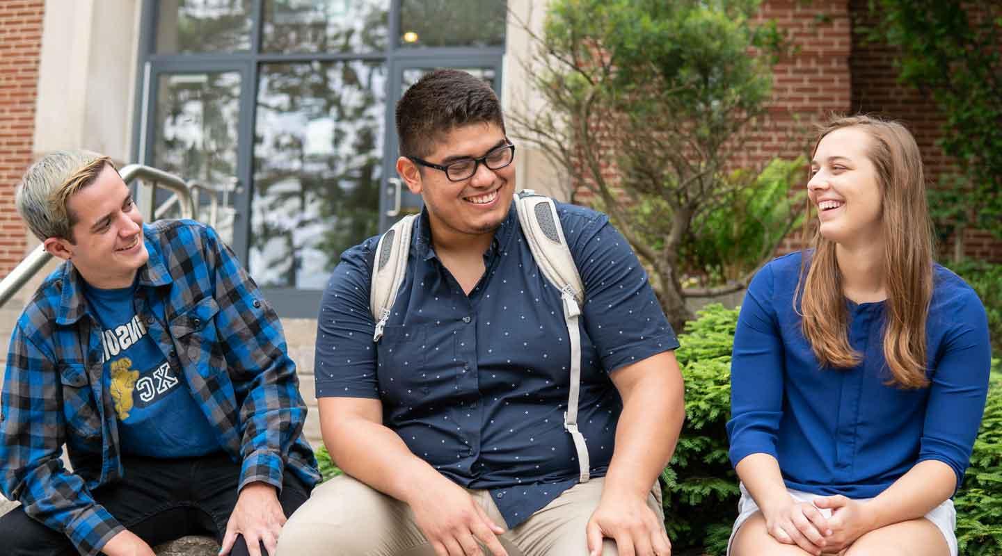 students laughing outside of a residence hall sitting down